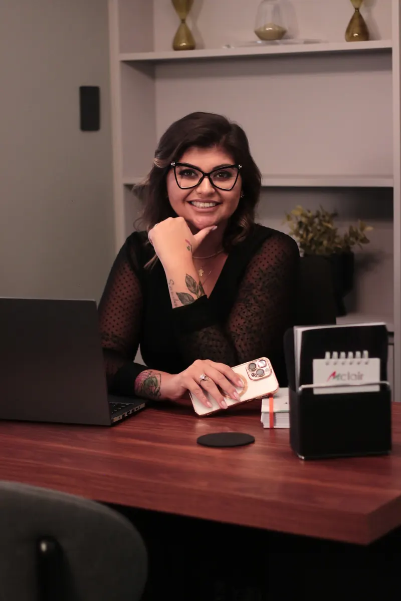 Kelly Pinheiro de óculos, sorrindo com a mão no queixo, à mesa do escritório da Mclair